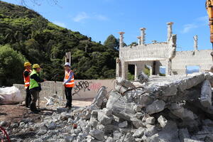 Three men in high vis vests and helmets stand in the shell of a demolished building.