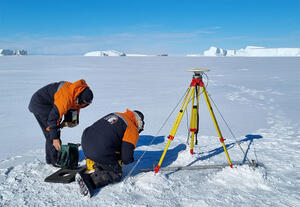 Two people using survey equipment on the ice field at McMurdo sound in Antarctica