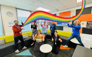 A group of coworkers smiling and pretending to hold up a rainbow
