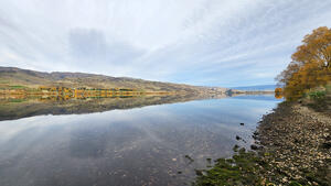 View across part of Lake Dunstan with the surface of the lake mirroring the sky and land