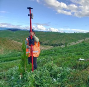 Person in hi-vis jacket holds a pole scanner, whilst standing in a rural valley