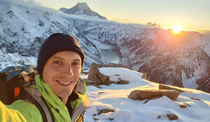 Alistair Collow, geospatial student, standing on a snowy mountain with sunrise in the background