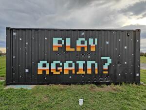 Artwork on a shipping container. Text says "Play again?"