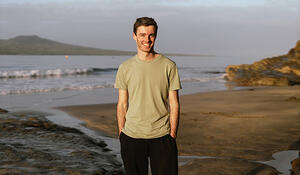Geospatial student Jordan Stewart standing in front of a beach and island
