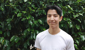 Geospatial student Samuel Wong standing in front of a leafy green background