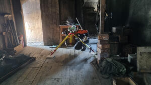 A surveyor crouched behind their equipment, in the middle of a historic hut